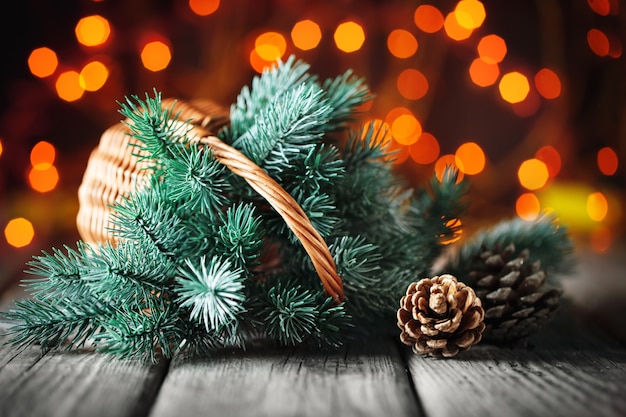 Cesta con ramas del árbol de Navidad en una mesa de madera en el fondo de una guirnalda