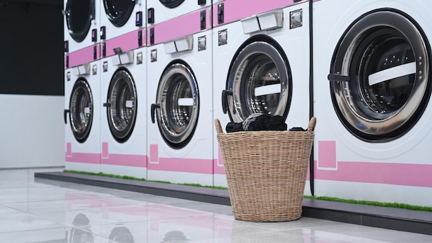 Una cesta de ropa cerca de la fila de lavadoras Instalaciones de lavandería de autoservicio