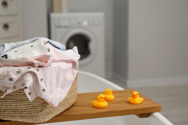 Cesta de ropa con ropa de bebé en la bandeja de la bañera en el primer plano del baño Espacio para texto