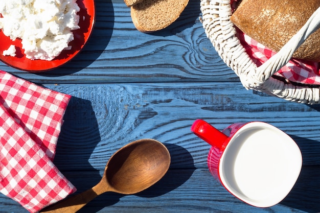 Cesta, una taza de leche, requesón y pan sobre una mesa de tablas azules. Vista superior