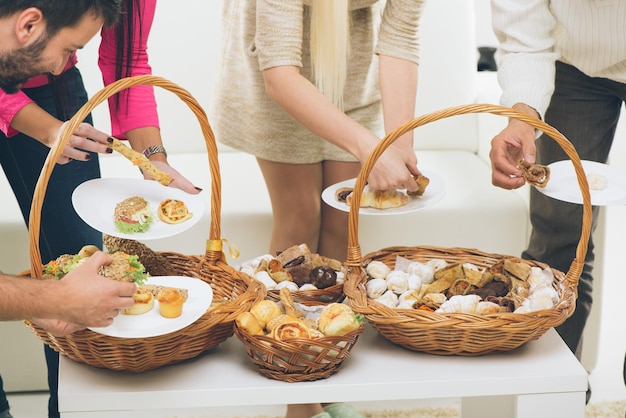 Cestas tejidas de primer plano llenas de productos horneados a los que un montón de manos se acercan para tomar el delicioso pastel.