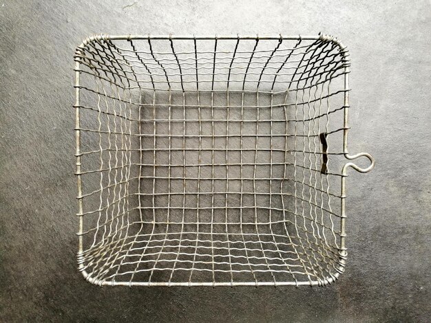 Foto cesto de arame vazio de prata com uma estrutura de grade quadrada em um chão de concreto cinza na cozinha