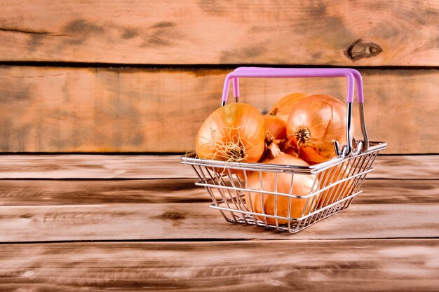 Cesto de compras com cebola na mesa de madeira.