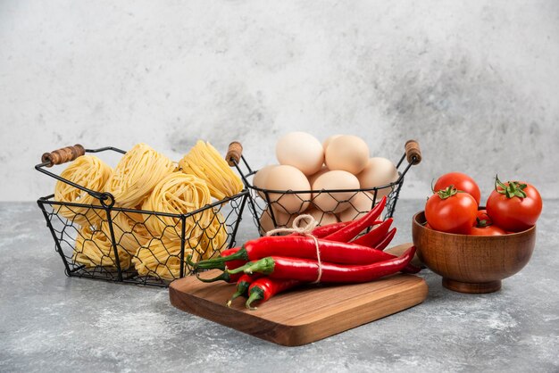 Cesto de macarrão cru tomates pimentas e ovos em superfície de mármore