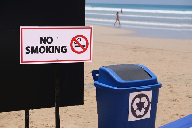 Foto cesto de reciclagem na praia e sinal de proibição de fumar