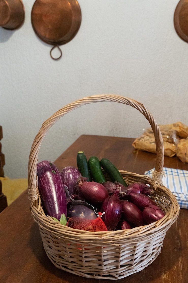 Foto cesto de vime cheio de legumes, berinjelas, abobrinhas e cebolas interior da cozinha