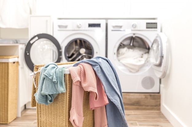 Cesto de la ropa sucia con lavadoras y secadoras en el fondo