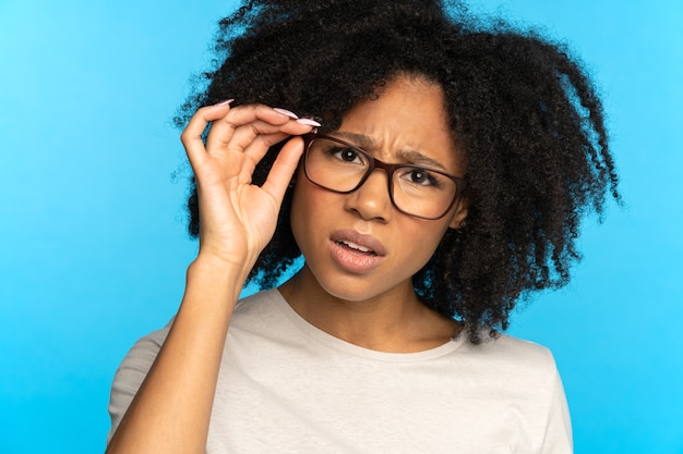 Cética e desconfiada garota afro-americana ajusta os óculos desconfiada olhando para a câmera