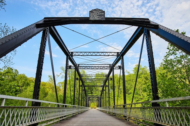 Céu azul brilhante com nuvens brancas sobre ponte de metal preto fundo de floresta verde exuberante