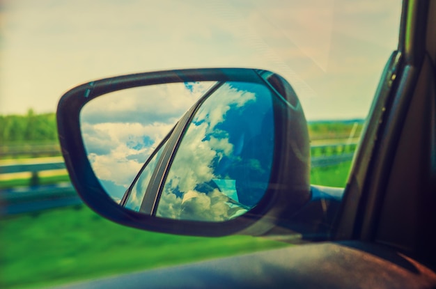 Céu azul com nuvens no espelho lateral de um carro na zona rural viajar conceito de advanture natural