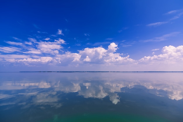 Céu claro azul com nuvens brancas refletidas nas águas calmas do mar em dia ensolarado