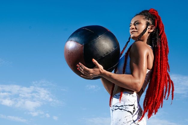 Céu de fundo. Mulher atlética com bola médica. Força e motivação. Foto de mulher desportiva em roupas esportivas da moda