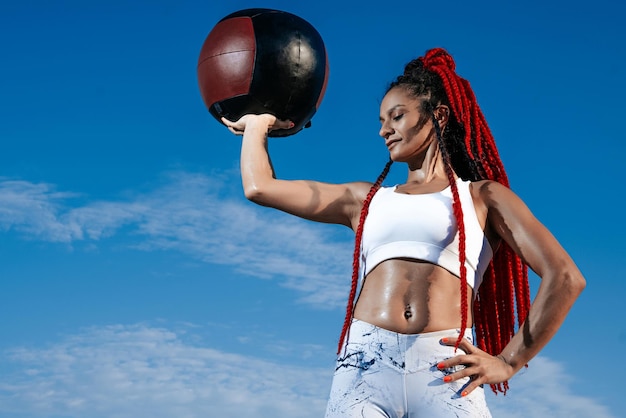 Céu de fundo Mulher atlética com bola médica Força e motivaçãoFoto de mulher esportiva em roupas esportivas da moda