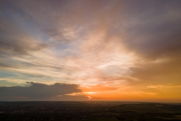 Foto céu de pôr-do-sol colorido e brilhante com sol a pôr e nuvens vibrantes sobre a paisagem escura