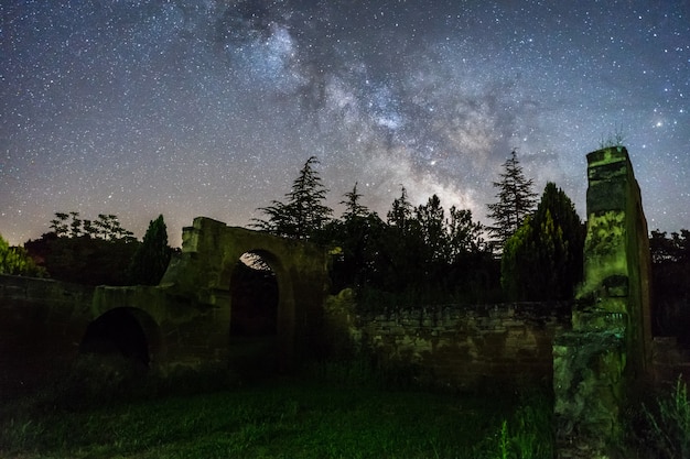 Céu noturno com a via láctea acima da floresta e ruínas na espanha