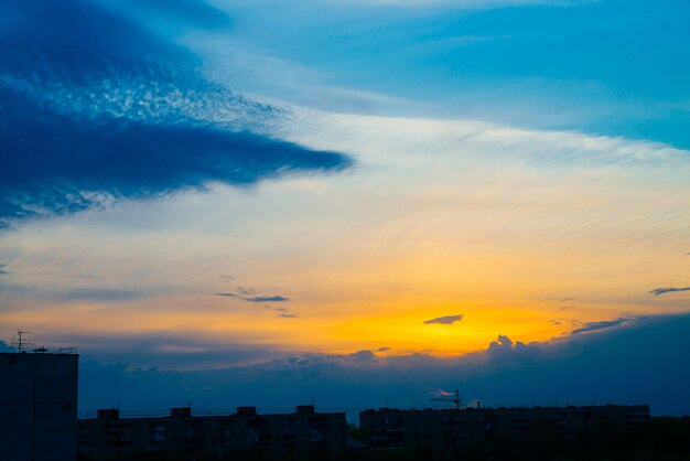 Céu nublado azul atmosférico por trás das silhuetas dos edifícios da cidade. Fundo cobalto e laranja do nascer do sol com nuvens densas