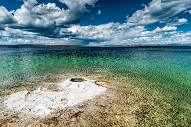 Foto céus chuvosos sobre o lago yellowstone e o pequeno gêiser de fishing cone no parque nacional de yellowstone