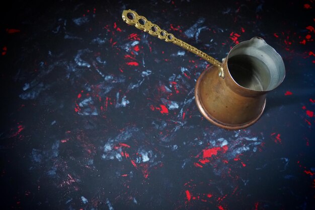 Cezve dos Balcãs para café turco Cezve de cobre em superfície preta Utensílios antigos de bronze Cabo de metal esculpido com padrão Fundo preto com manchas brancas vermelhas e azuis