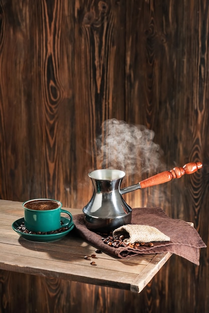 Cezve e xícara com café quente na mesa de madeira