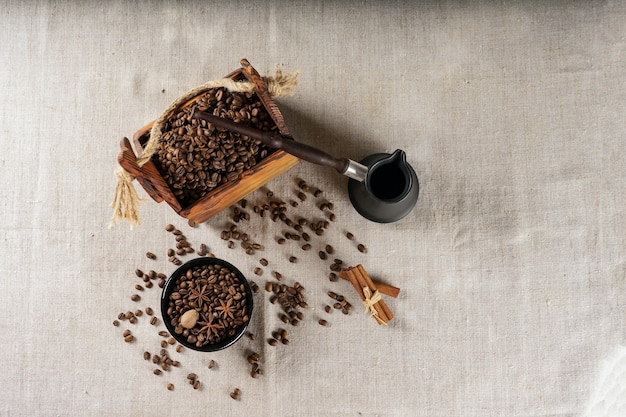 Cezve und geröstete Kaffeebohnen in einer Schachtel auf einem rustikalen Tisch, Zimt und getrockneter Zitrone.