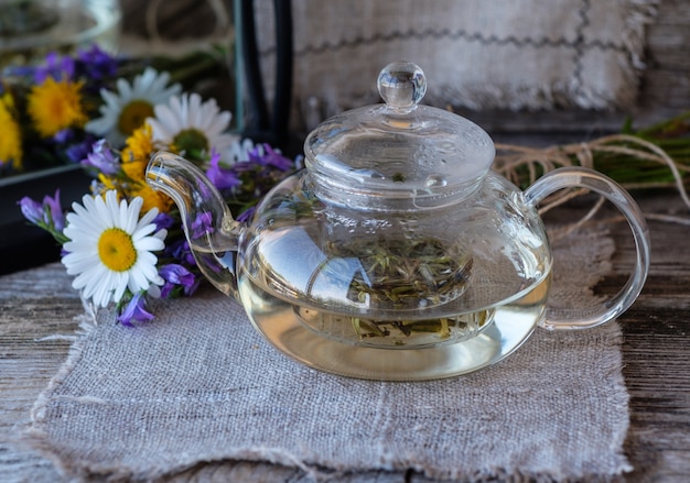 Chá branco chinês da província de Financiamento em um bule de vidro sobre uma mesa de madeira com flores do campo e um espelho