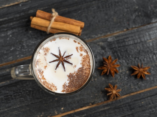 Chá caseiro latte com canela e anis em fundo preto rústico de madeira em caneca de vidro