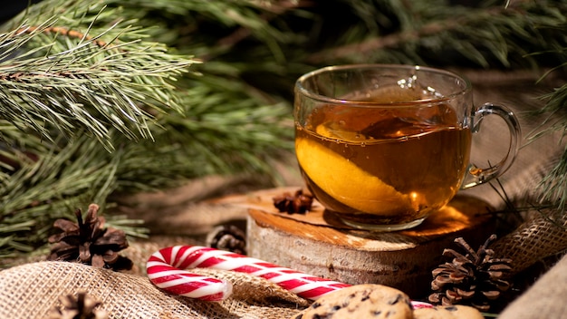 Chá com limão, ao lado de biscoitos e pirulito em serapilheira e galhos de árvore de natal e cones.