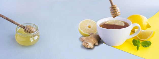 Chá com mel de limão e gengibre na xícara branca sobre fundo cinza e amarelo Copiar espaço