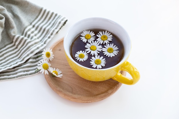 Chá de camomila em uma xícara amarela em um pires de madeira Flor de camomila na superfície do chá Espaço de cópia de fundo branco