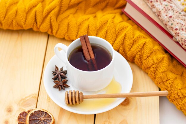 Chá de canela quente aromático coberto com um cachecol quente em um fundo de madeira de outono mergulhador de mel com mel confortável lendo um livro