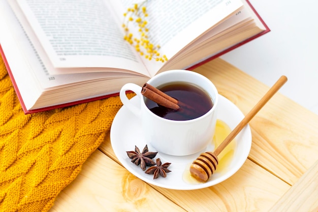 Chá de canela quente aromático coberto com um cachecol quente em um fundo de madeira de outono mergulhador de mel com mel confortável lendo um livro
