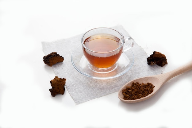 Chá de chaga em um copo de vidro e pedaços de chaga em um fundo claro