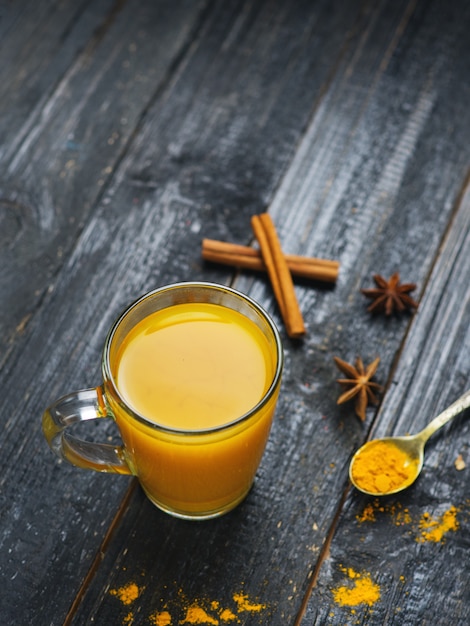 Chá de cúrcuma em uma xícara de canela em um fundo escuro de madeira