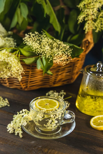 Chá de ervas de flor de sabugueiro rodeado de flores frescas e folhas em cesta estilo rústico escuro Fechar