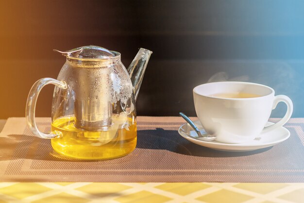Chá de ervas em um bule de vidro e uma xícara branca em uma mesa ao ar livre