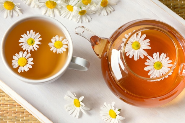 Chá de ervas em xícara de flores de camomila e bule na bandeja de madeira branca