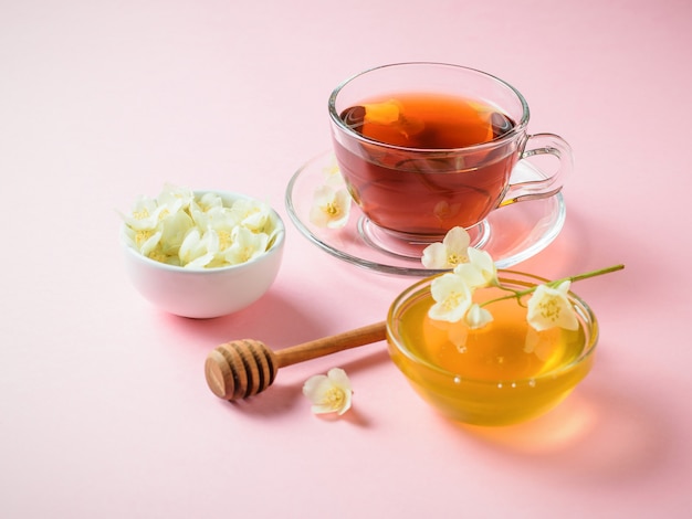 Chá de ervas, mel, flores de jasmim e uma colher de pau em uma mesa-de-rosa. a composição da manhã café da manhã.