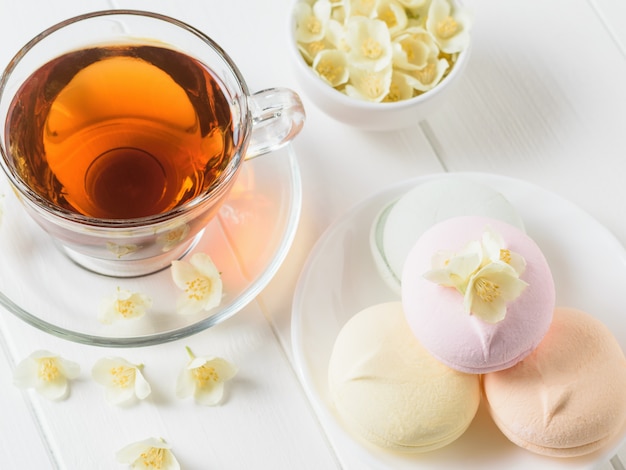 Chá de ervas, uma tigela de marshmallows e uma tigela de flores de jasmim em uma mesa branca