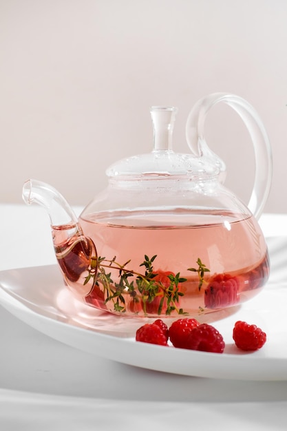 Chá de ervas vermelhas com tomilho e framboesa fresca em bule de vidro. fundo branco com copyspace