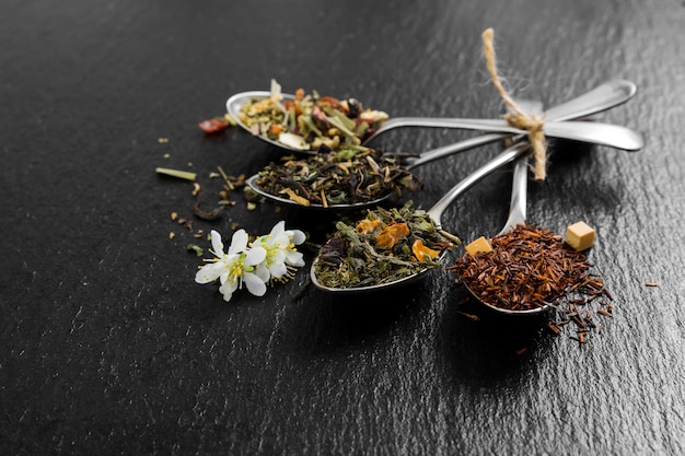 Chá de flores aromáticas em colher de metal em fundo pretoxA