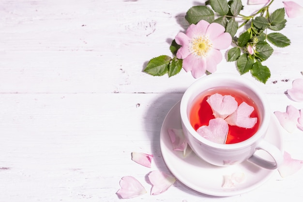 Chá de flores de rosa mosqueta. Bebida vitamínica de verão, luz forte, sombra escura. Fundo de madeira branco, copie o espaço