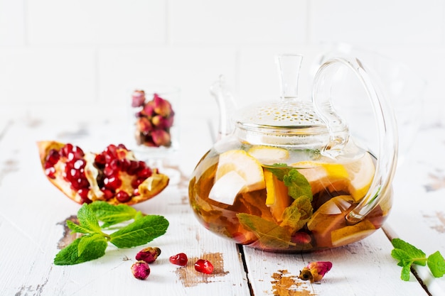 Chá de frutas com frutas vermelhas, limão, limão e folhas de hortelã em um bule de vidro