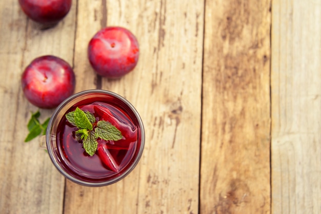 Chá de frutas vermelhas em copo de vidro com ameixas na mesa de madeira.