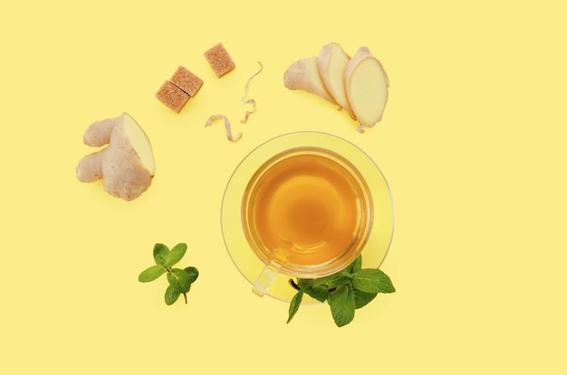 Chá de gengibre com limão em copo de vidro com açúcar orgânico marrom e hortelã em fundo de papel amarelo