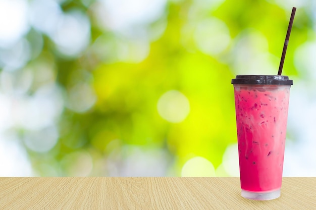 Chá de leite rosa com gelo sobre fundo verde da natureza Bebidas de verão com gelo