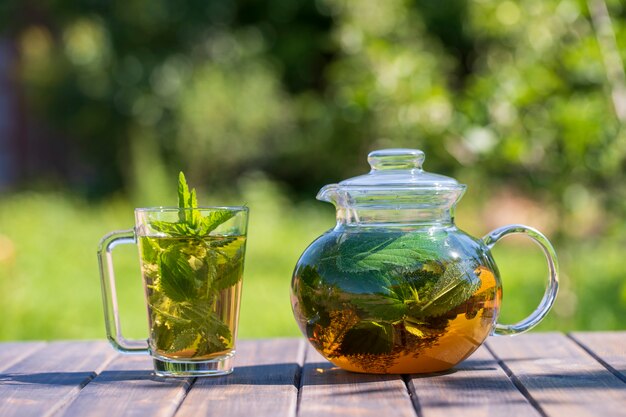 Chá de urtiga saudável em um bule de chá de vidro e uma caneca no jardim de verão na mesa de madeira