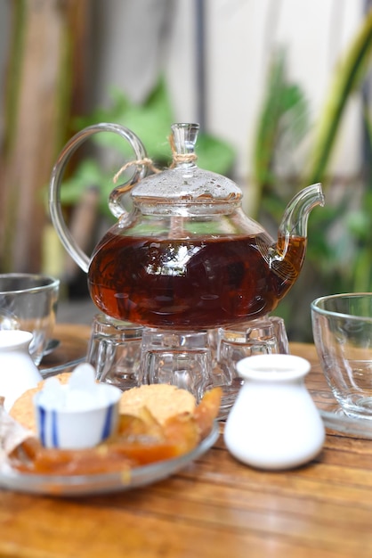 Chá Earl Grey em bule de vidro com xícaras e frutas cristalizadas na mesa de madeira