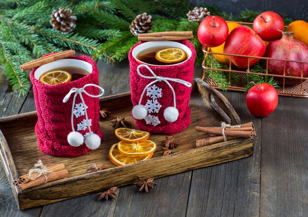 Chá em uma caneca com decoração de malha, fatias de laranja, cesta de frutas, canela, ramos de abeto