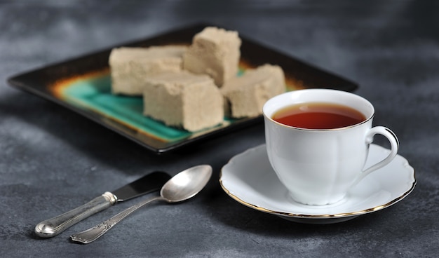 Chá em uma caneca com uma borda dourada e um pires e halva cortados em pedaços