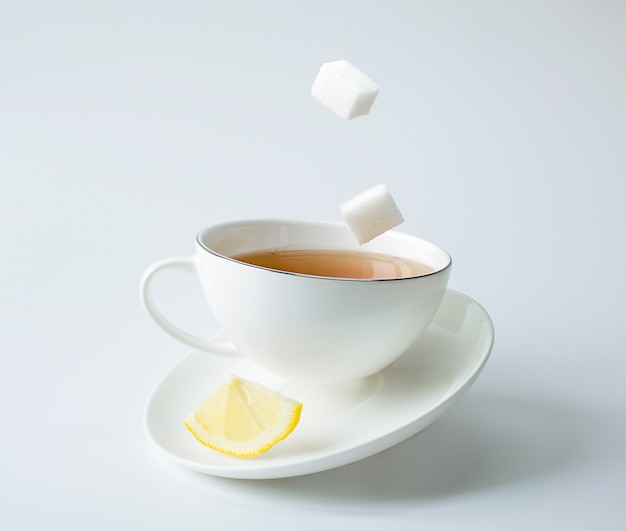 Chá em uma xícara branca com limão e açúcar. equilíbrio e levitação.